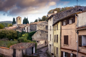 Lane in the village of Félines Termenès in autumn with view at the tower of the church Notre Dame Lane in the village of Félines Termenès in autumn with view at the tower of the church Notre Dame